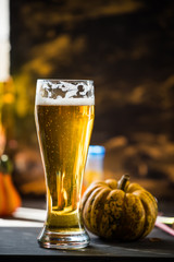 glass of golden beer on dark, wooden table, surrounded by autumn decorations, pumpkins, leaves