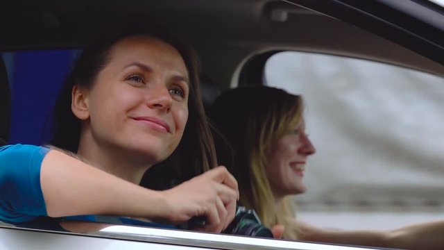 Two young women ride in a car and have fun. One of them takes a self photo on a film camera. Slow motion