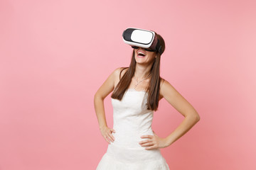Laughing bride woman in white wedding dress and headset of virtual reality standing with arms...