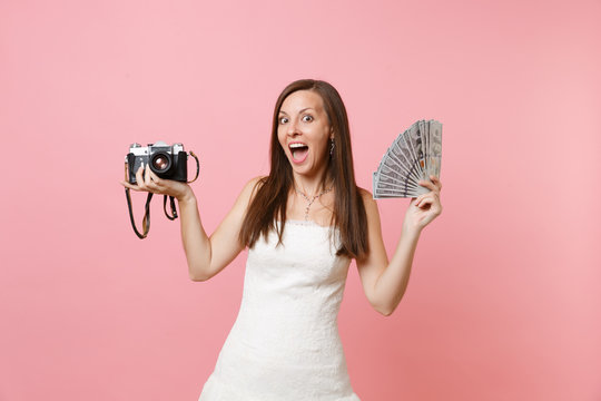 Excited happy bride woman in wedding dress hold retro vintage photo camera bundle lots of dollars cash money choosing staff, photographer isolated on pink background. Organization, Wedding to do list.