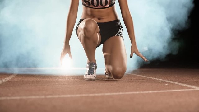 Asian Athlete ready to start. Young female runner preparing for blasting off in mist on sports track of stadium, training before competition 4k