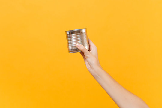 Close Up Female Hold In Hand Clear Empty Blank Iron Metal Chrome Can Canned Goods Food Isolated On Yellow Background. Packaging Template Mockup. Delivery Service Concept. Copy Space. Advertising Area.