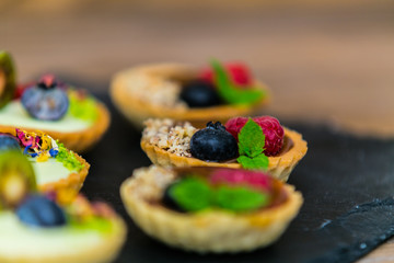 Homemade shortbread tartlets with custard cream and fruit..Tartlets dessert, pastry cakes with fresh fruit on wooden background