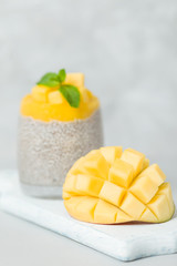 Chia seeds pudding with mango puree in beautiful glasses with green mint leaves and cut fresh ripe tropical fruit.