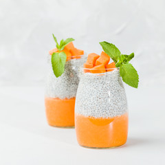 Chia seeds pudding with pumpkin puree in beautiful glasses with green mint leaves and cut fresh ripe orange vegetable.