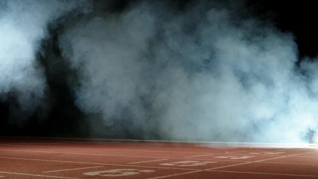 Runner heading forward. Young female athlete blasting off in smoke on short track of stadium, training before olympics 4k