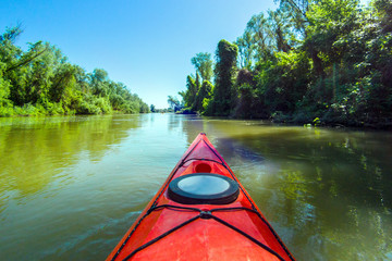 Bow of red kayak in Danube river and a green summer forest in the background.