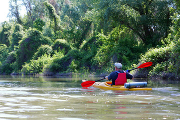 Man paddles a yellow kayak on Danube river near thickets of wild grapes. Summer kayaking