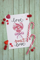 postcard for valentines on old green wooden background with red candies and lollipop
