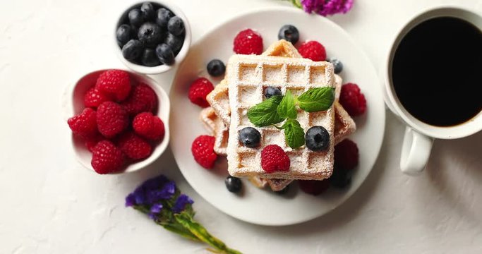 From above shot of cup of aromatic coffee and bowls with fresh berries standing near plate with delicious soft waffles