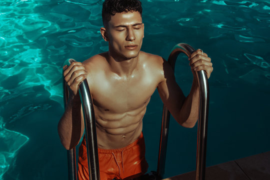 Strong face muscle male model in the open  summer shower on the vacation pool background with blue water on the nature beach on the sunset