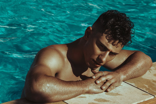 Strong face muscle male model in the open  summer shower on the vacation pool background with blue water on the nature beach on the sunset