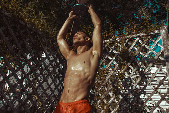 Strong face muscle male model in the open  summer shower on the vacation pool background with blue water on the nature beach on the sunset