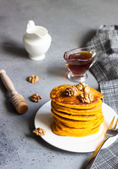 Pumpkin pancakes with maple syrup or honey and walnuts on a white plate. Grey concrete. Copy space....