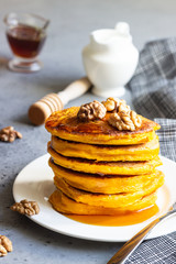 Pumpkin pancakes with maple syrup or honey and walnuts on a white plate. Grey concrete. Copy space. Healthy breakfast. Autumn food.