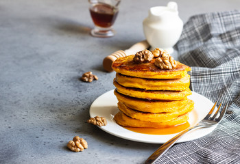 Pumpkin pancakes with maple syrup or honey and walnuts on a white plate. Grey concrete. Copy space. Healthy breakfast. Autumn food.