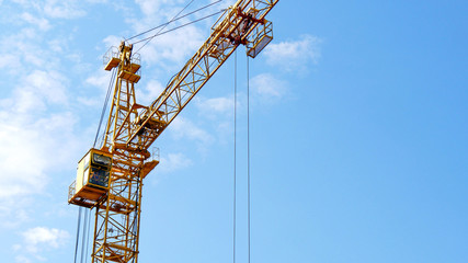 The building crane near the building under construction against the blue sky