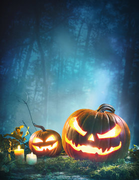 Jack o’ lanterns glowing at moonlight in front of spooky forest