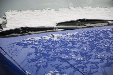 Blue car covered with melting snow. Closeup. Selective focus on the snow over wipers. Driving in winter concept.