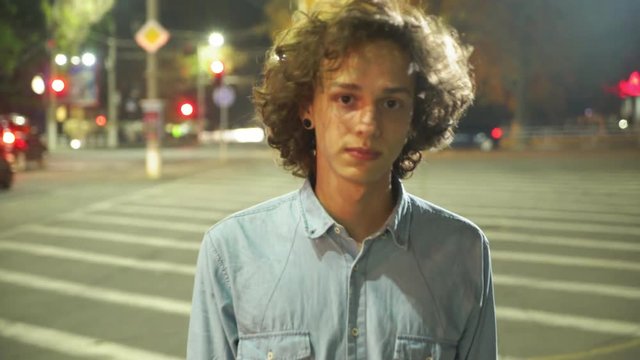  Arty view of a young man with long wavy hair going along a zebra crossing and smiling cheerfully in a city street at night in autumn  