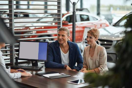 Happy Positive Caucasian Couple Signing Sale Contract At Car Dealer Office, Talking With Sales Person About Vehicle Insuarance