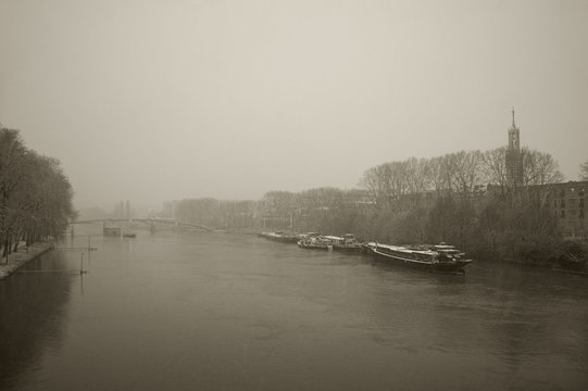 Houseboats in snowfall on the river Marne flowing through Parisian suburbs. Flooded banks. Evening misty dusk. Blurry snow flake motion. Sepia photo.