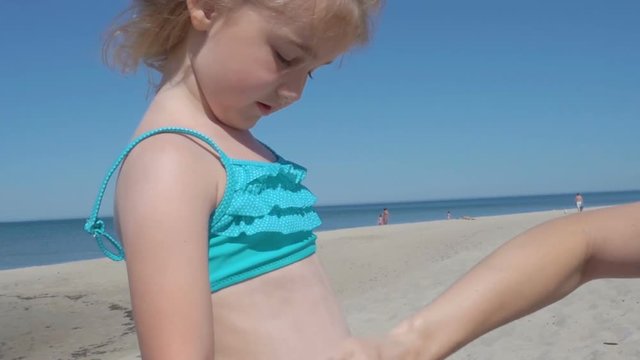 Mother applying sunscreen lotion on Daughter  at beach. Mother preparing child for bath in sea.
