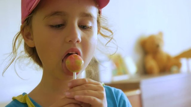 Little girl enjoying a lollipop while staring at camera. Child eating candy, sweets, sugar