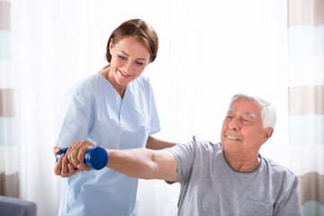 Obraz premium Nurse Helping Senior Man With Dumbbell Exercise