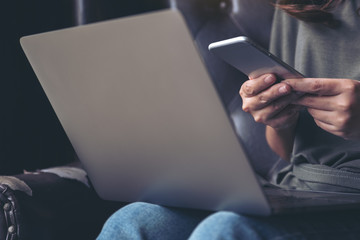 A woman holding and using mobile phone while working on laptop