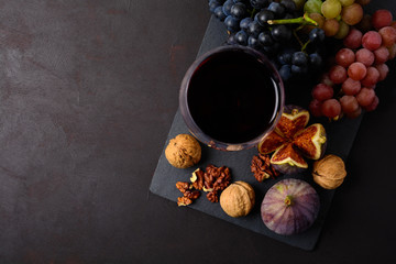 Obraz na płótnie Canvas Wineglass with red wine, grapes, figs and walnuts lying on dark wooden background. Top view. Flat lay. Copy space