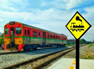 Obraz premium focus on train icon yellow warning road sign with blurred background of train is running on railroad tracks with clouds and blue sky background 