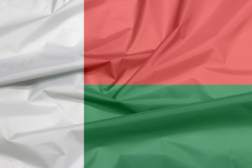 Obraz premium Fabric flag of Madagascar. Crease of Madagascar flag background, Two horizontal bands of red and green with a white vertical band on the hoist side.