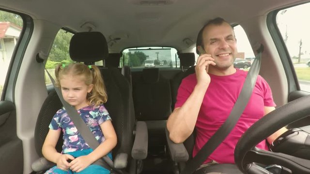 Father and his little daughter are driving in the car. A bad parent uses a smartphone while driving a car. Man talking on the phone while driving  with his daughter in the car.
