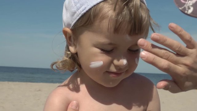 Sun protection. Mother anoints her son face protective cream on the beach. Family vacation at the sea. Slow motion.  Portrait of little boy in suncream