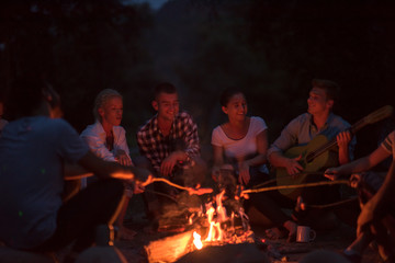 young friends relaxing around campfire