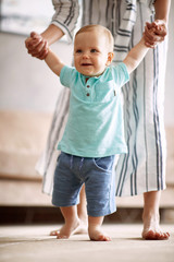 Cute baby boy making first steps with mother.