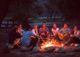 young friends relaxing around campfire - obrazy, fototapety, plakaty