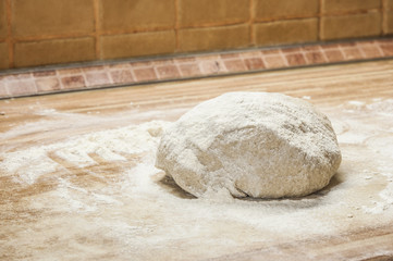 Whole wheat pizza dough shaped into ball on floured wooden background