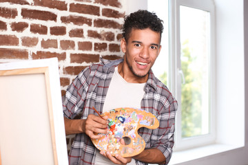 Young African-American artist painting picture in workshop