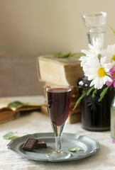 Cream de Cassis homemade blackcurrant liqueur in small glasses, books and flowers. Rustic style.
