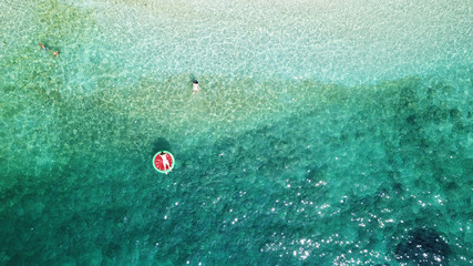 Aerial drone photo of couple playing with inflatable watermelon in tropical bay with emerald sea