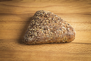Triangle-shaped wholemeal bread with flax seeds, oats and sesame on a wooden table
