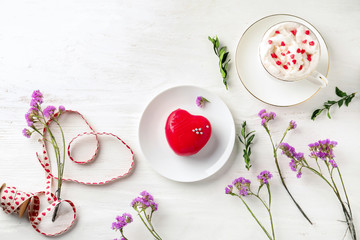 Composition with heart shaped dessert, cup of hot drink and flowers on white wooden background