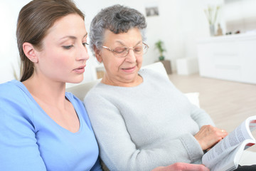 young female caregiver reading a story to the old woman