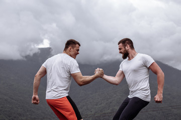 Two caucasian athletes in sportive wear measuring forces at outdoor crossfit training, over misty wooden mountains view.