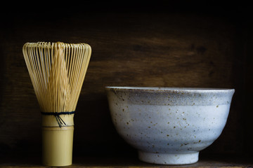Japanese matcha green tea whisk or chasen with a defocussed chawan or traditional ceramic bowl with dark creative lighting