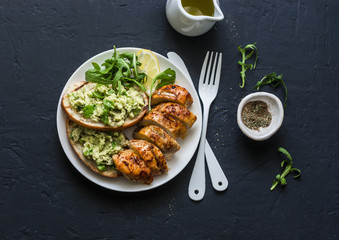 Roasted chicken breast and avocado toast - healthy lunch on a dark background, top view