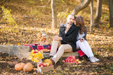 Beautiful couple in love in the fall at a picnic. Lovers are kissing, hugging, drinking tea. Steam and pumpkin, yellow leaves, tea. Copy space