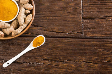Turmeric powder and fresh turmeric on wooden background
